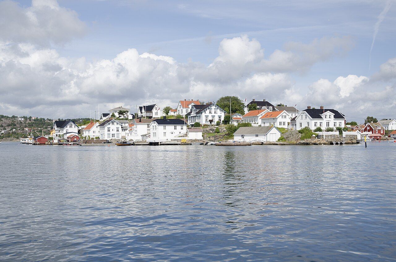 White wooden houses on a small island at Lyngør, reflected in calm water